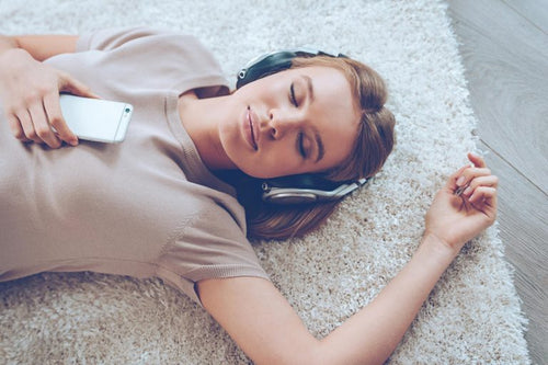 Young girl laying on a beige rug with music headphones on and eyes closed.