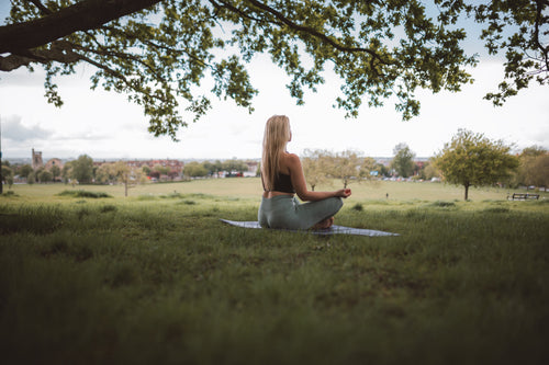 Blonde headed woman sitting in meditation under a green leaved tree
